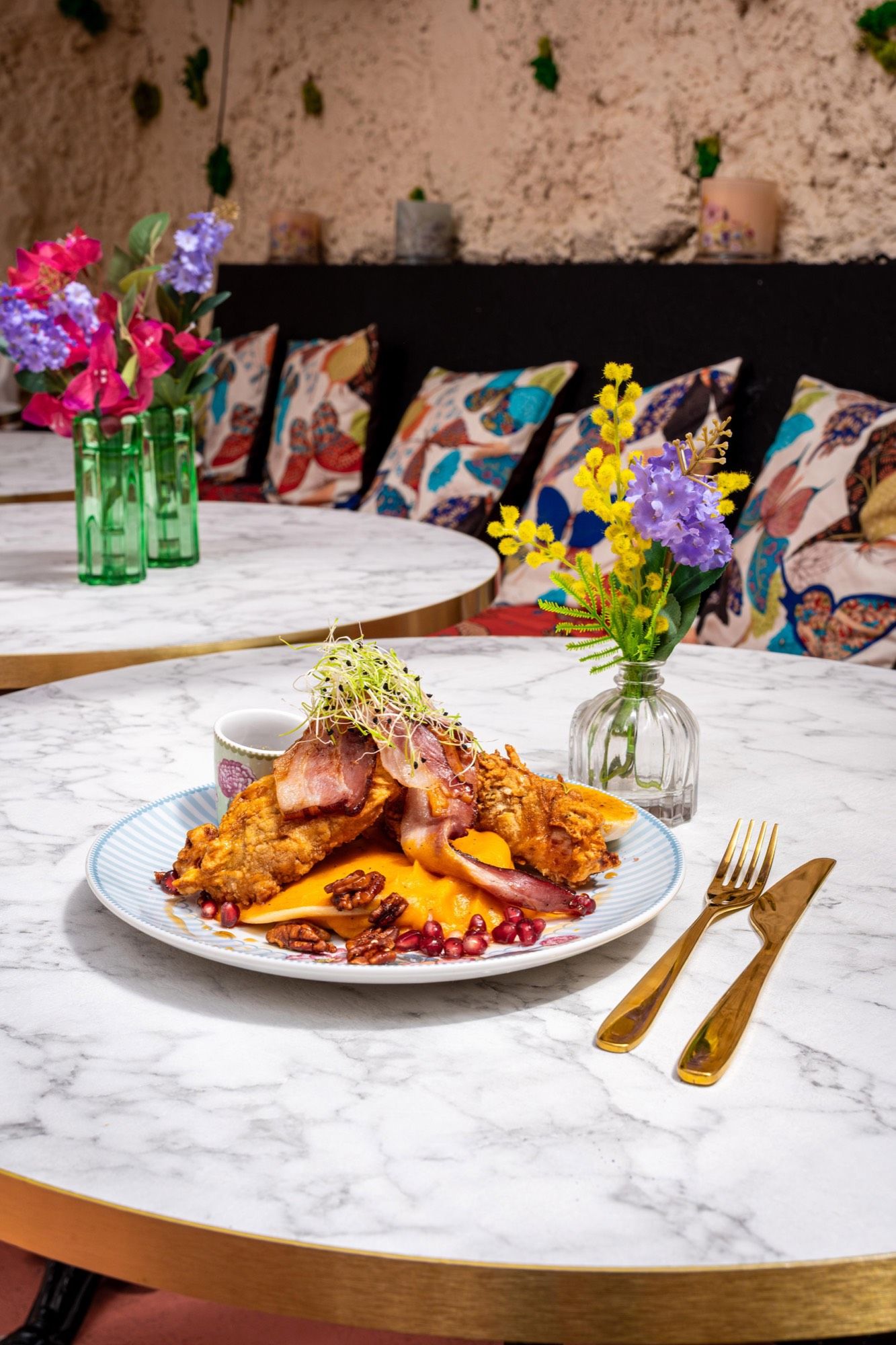 Une assiette servie dans la salle de PEACH — marbre, or et coussins colorés en arrière-plan